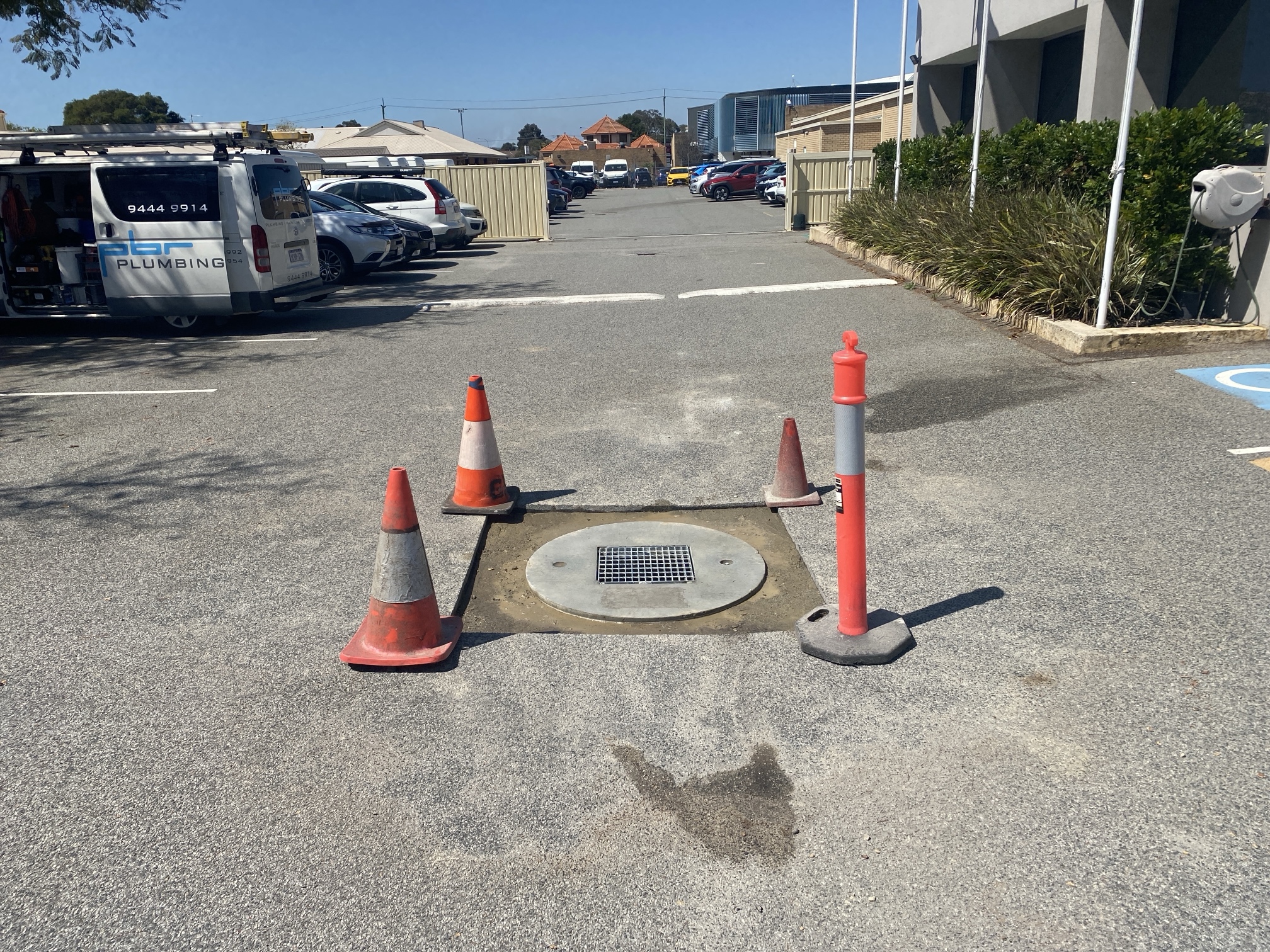 Soakwell access lid in a commercial carpark cordoned off with safety cones for maintenance inspection