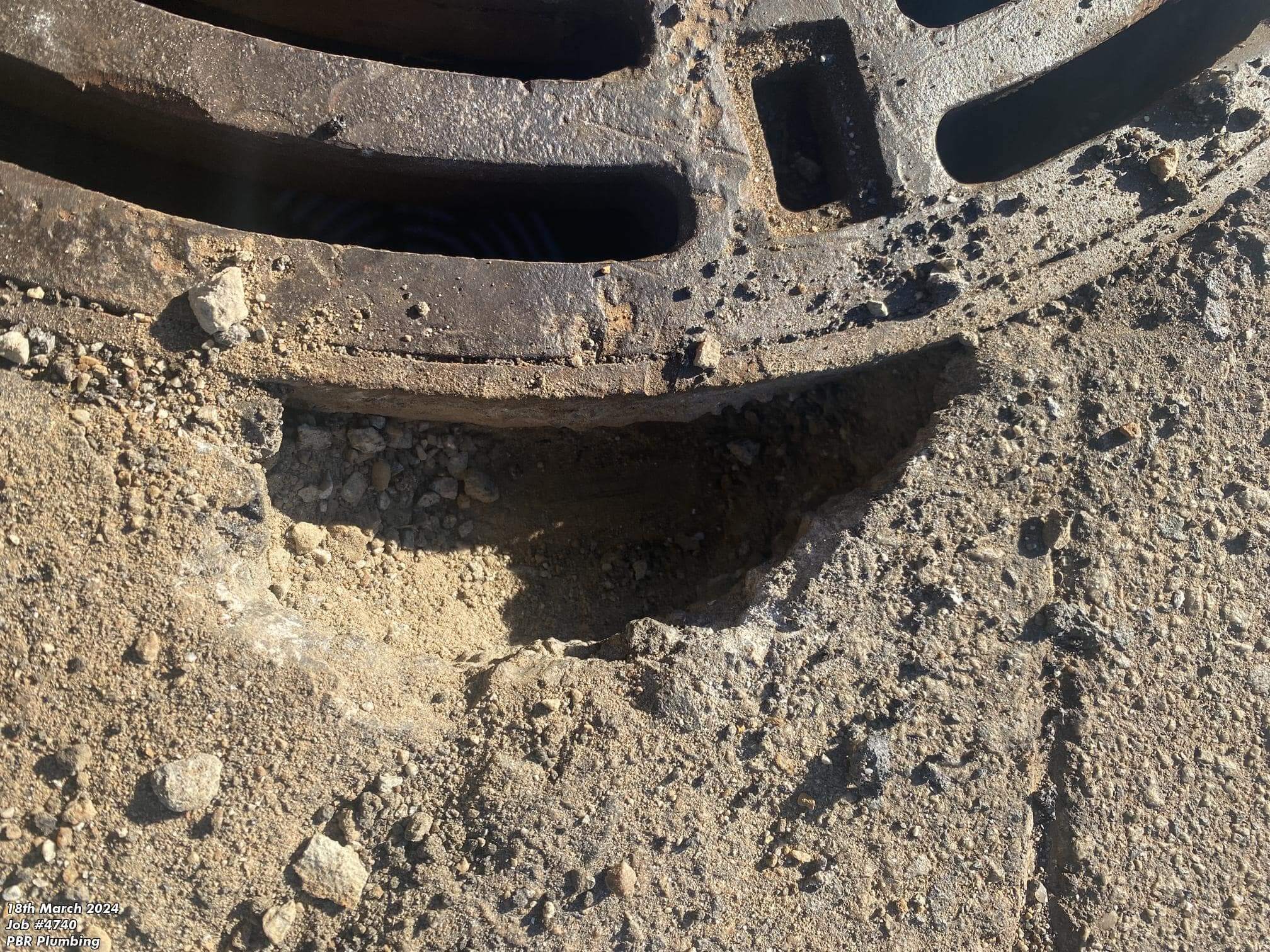 Rusted soakwell grate removed from the ground, exposing surrounding soil and drainage structure.