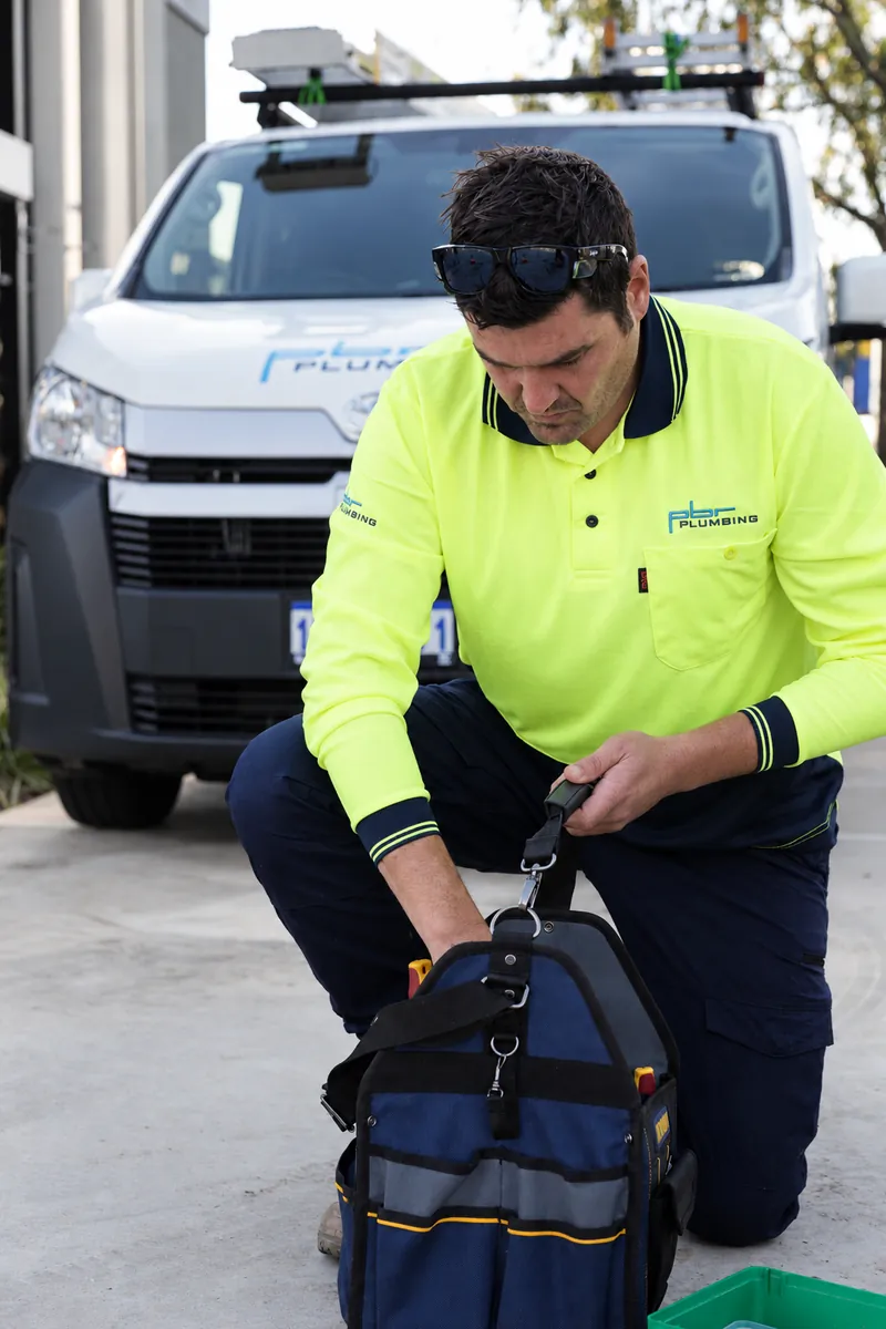 PBR plumber in hi-vis with a tool bag beside a service van