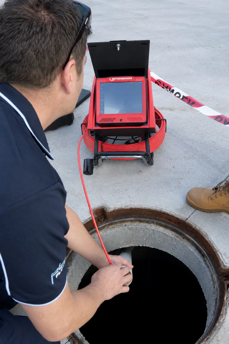 Plumber feeding a CCTV drain camera into an open manhole